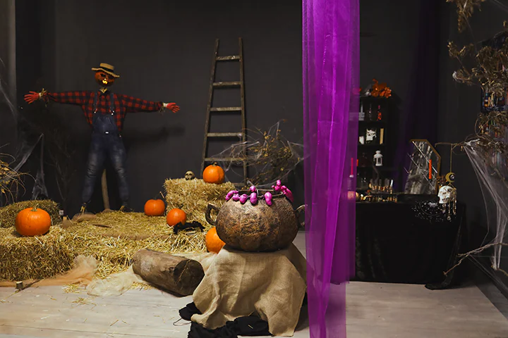 Общий план фотозоны на Хэллоуин с пугалом, тыквами и большим ведьминым котлом.