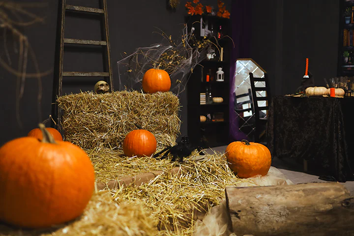 Крупный план оранжевых тыкв, лежащих на стогах сена в темной фотостудии, оформленной к Хэллоуину.